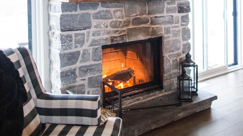 A cozy fireplace with a wooden mantle beside a comfortable chair, creating a warm and inviting atmosphere.