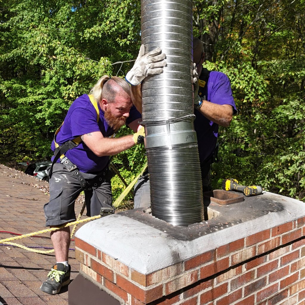 Two men in purple shirts collaborating on a chimney repair, demonstrating teamwork and skilled craftsmanship.