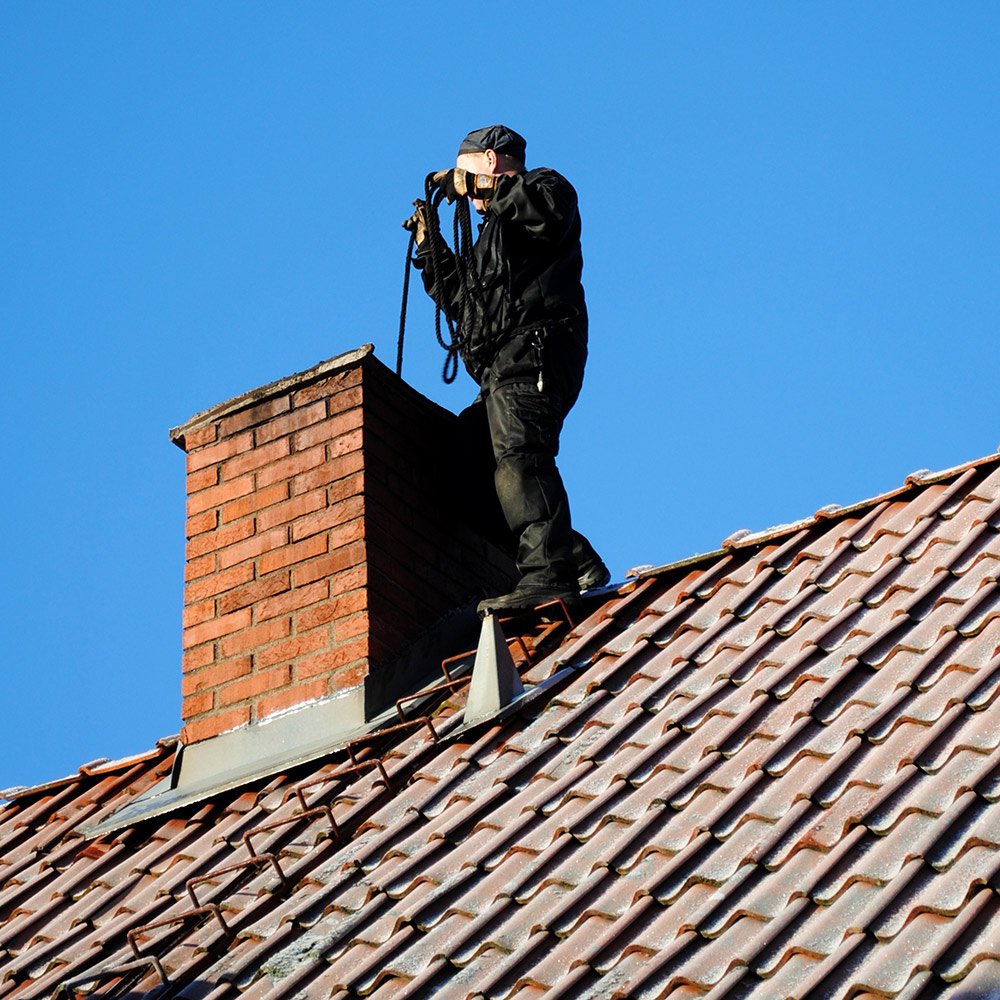 A man dressed in traditional chimney sweep attire, complete with a tall black hat and a soot-covered face, is seen climbing down a chimney.

