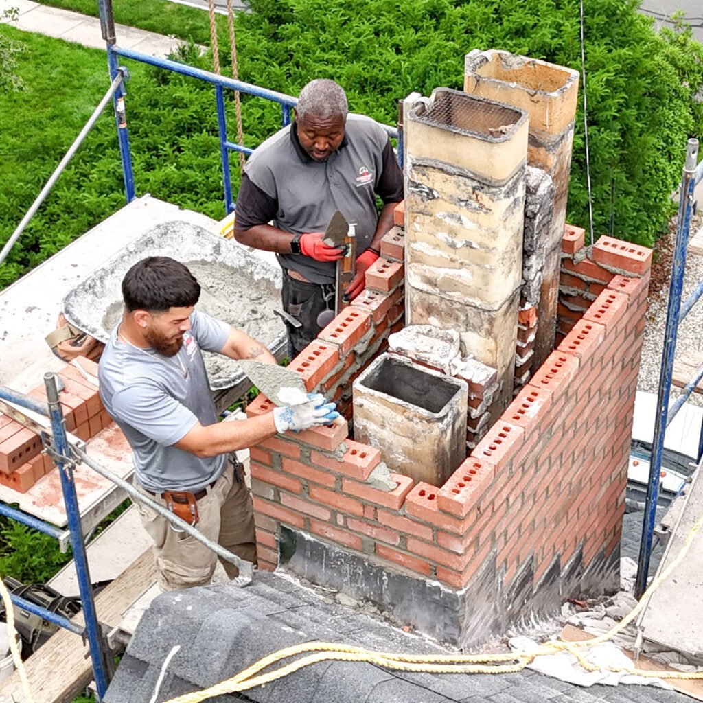 Two men collaborating on the construction of a brick chimney, demonstrating teamwork and skilled craftsmanship.