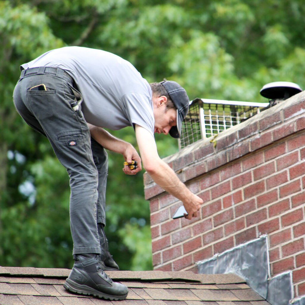 A man repairing a chimney on a rooftop, focused on his task amidst a clear blue sky.