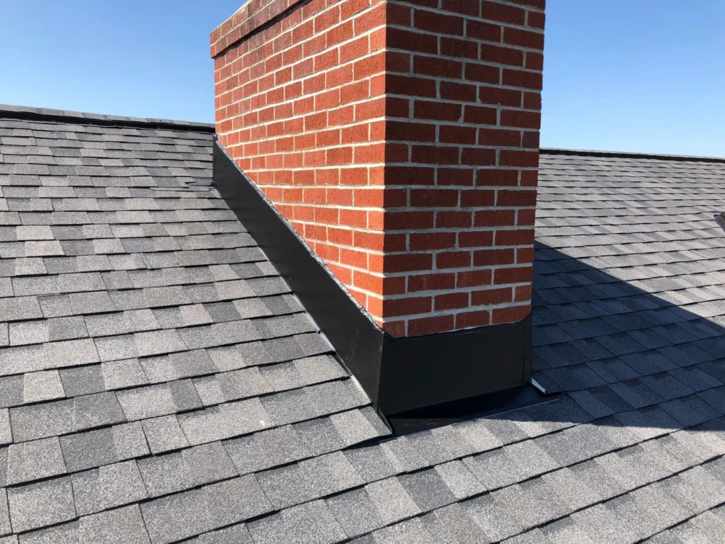 Close-up of a brick chimney with newly installed black flashing on a shingled roof, showcasing proper weatherproofing and protection against leaks